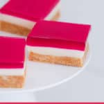 Pieces of raspberry jelly slice on a white cake stand.