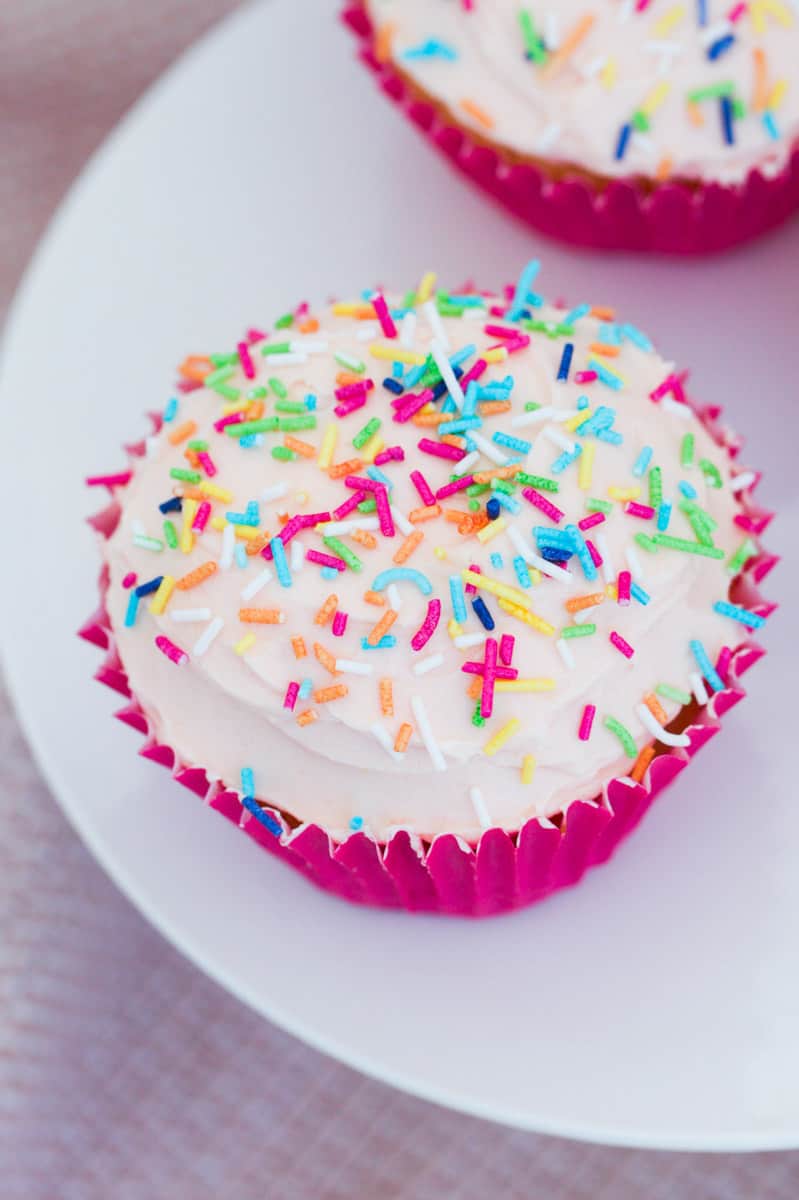 Sprinkles covering an iced white cupcake.