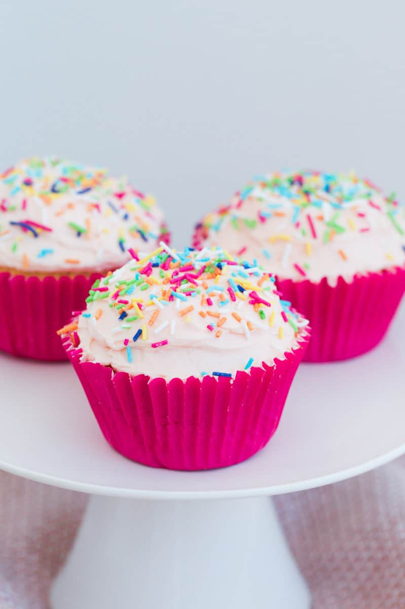 Three cupcakes covered with buttercream and sprinkles in pink cupcake cases.