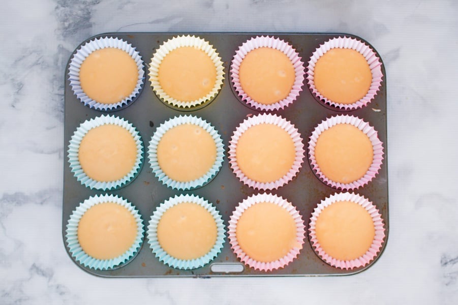 White cupcake mixture in paper cases in a muffin baking tray.