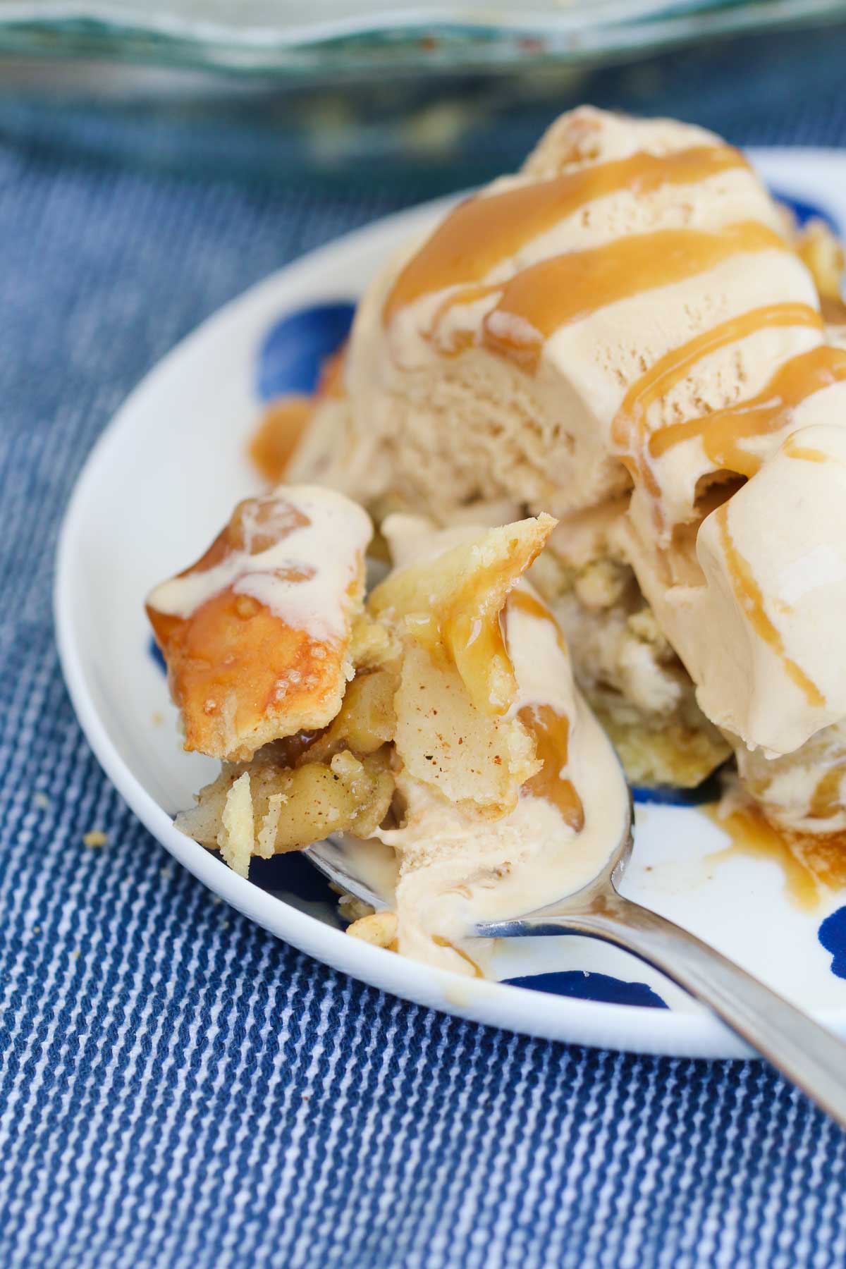 A spoonful of homemade apple pie on a spoon with ice-cream and caramel sauce.