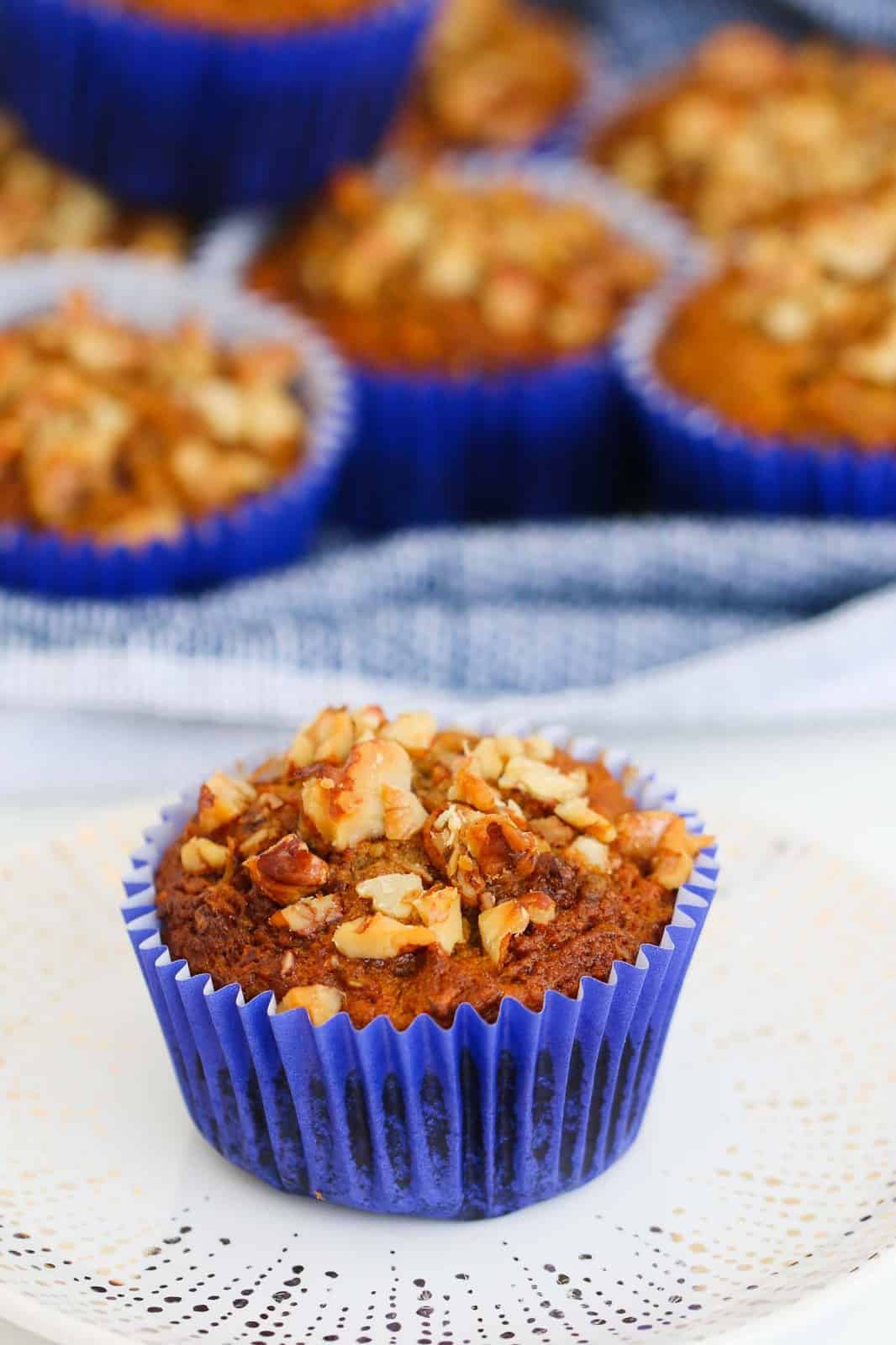 A healthy carrot cake muffin in a blue paper muffin case with nuts sprinkled on top, served on a plate.