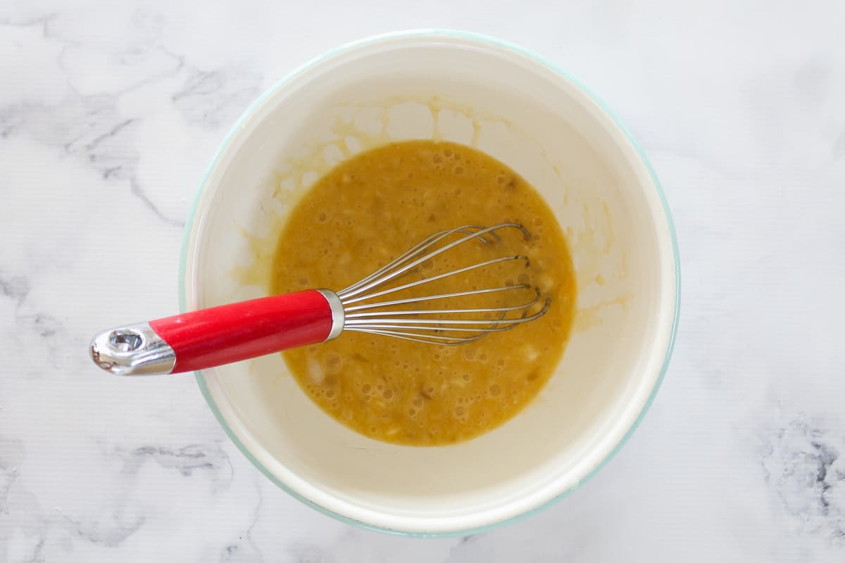Eggs, banana, coconut oil and honey mixed in a bowl with a whisk.