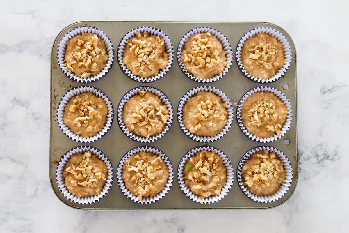 Filled muffin cases in a muffin tray, with chopped walnuts sprinkled on top.