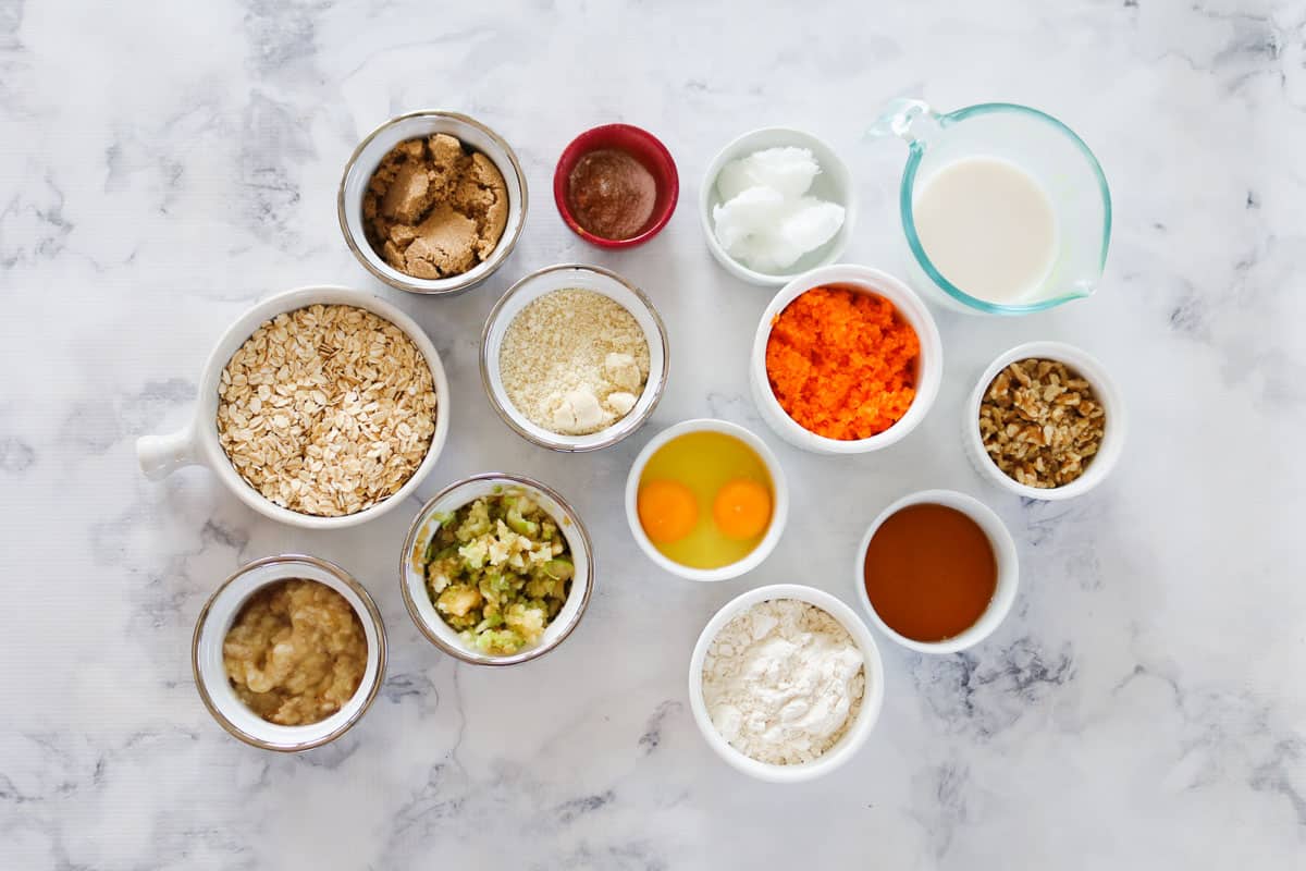 The ingredients for healthy carrot cake muffins in separate bowls on a marble bench