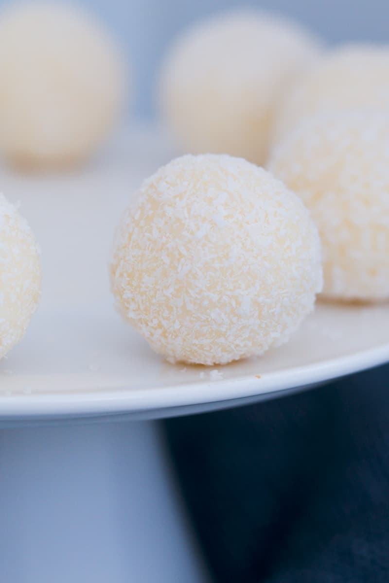 A white chocolate truffle coated in coconut on a cake plate. 