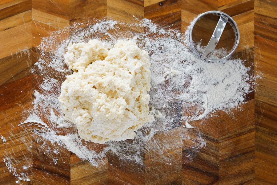 A scone cutter next to dough on a chopping board.