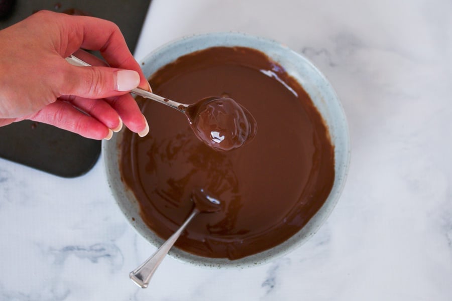 A spoon holding a chocolate cheesecake ball covered in chocolate.