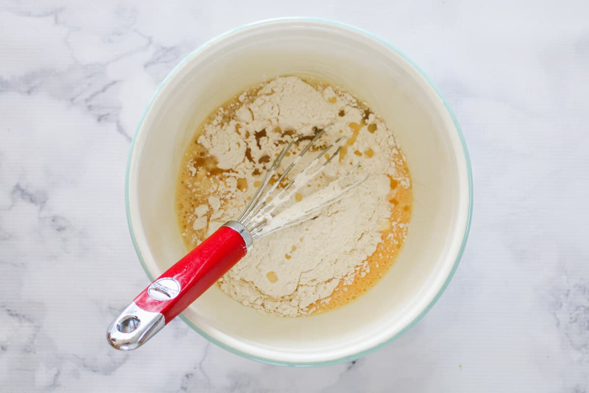 Flour and oil on top of beaten eggs in a mixing bowl.