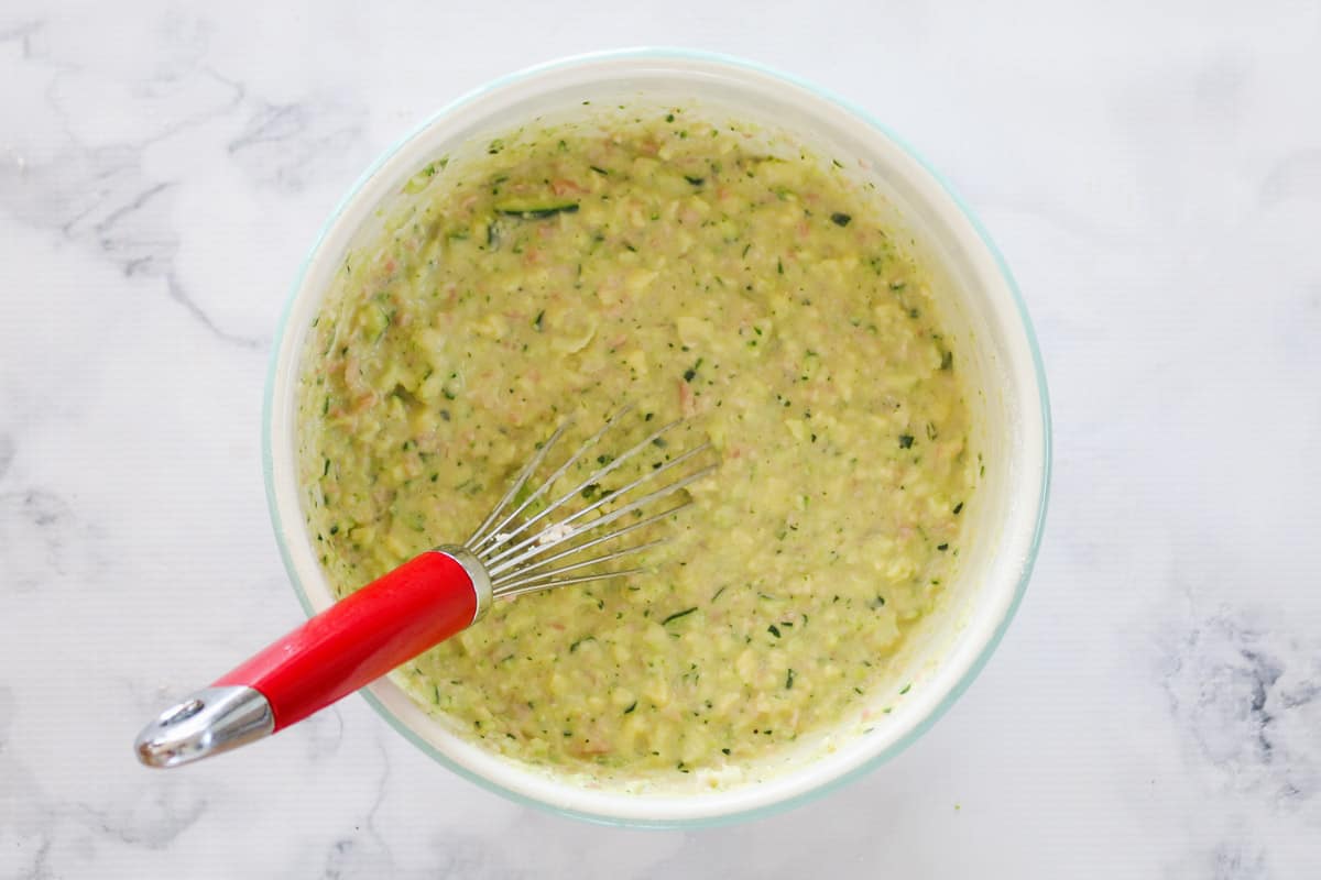 Zucchini slice mixture in a bowl with a whisk.