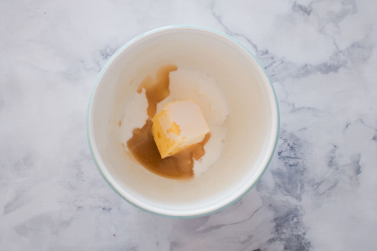 Butter, sugar and vanilla extract in a bowl on a marble bench.