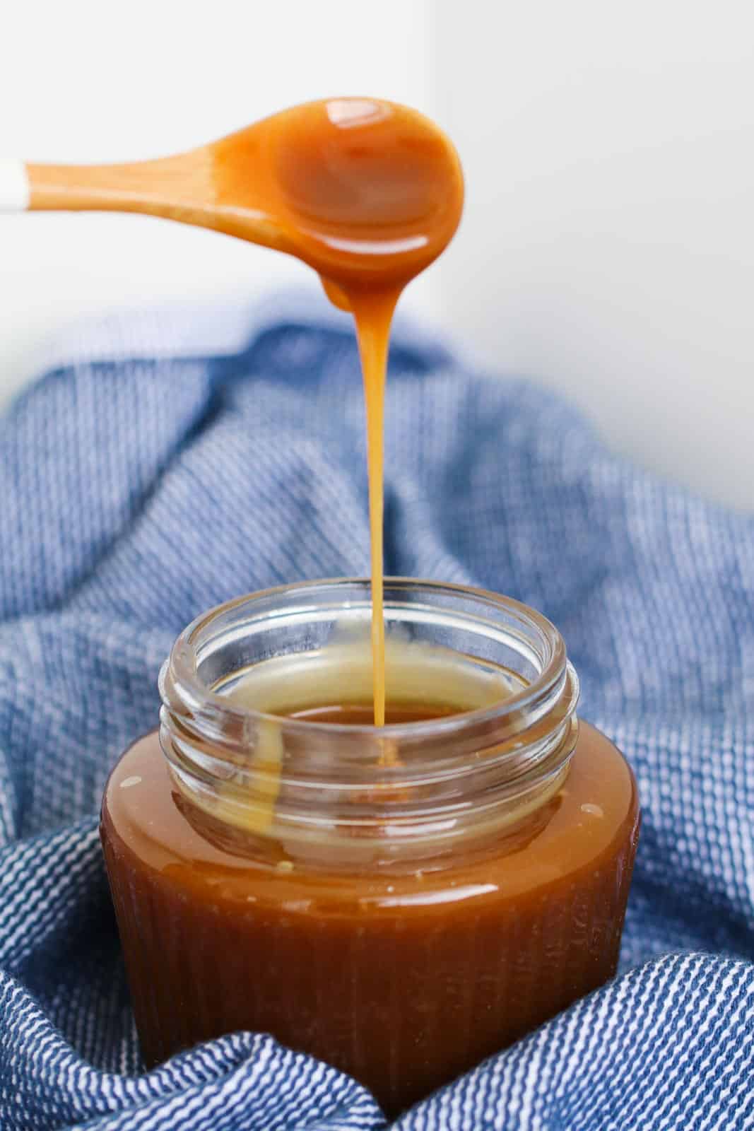 Caramel sauce dripping off a small spoon into a jar of sauce.