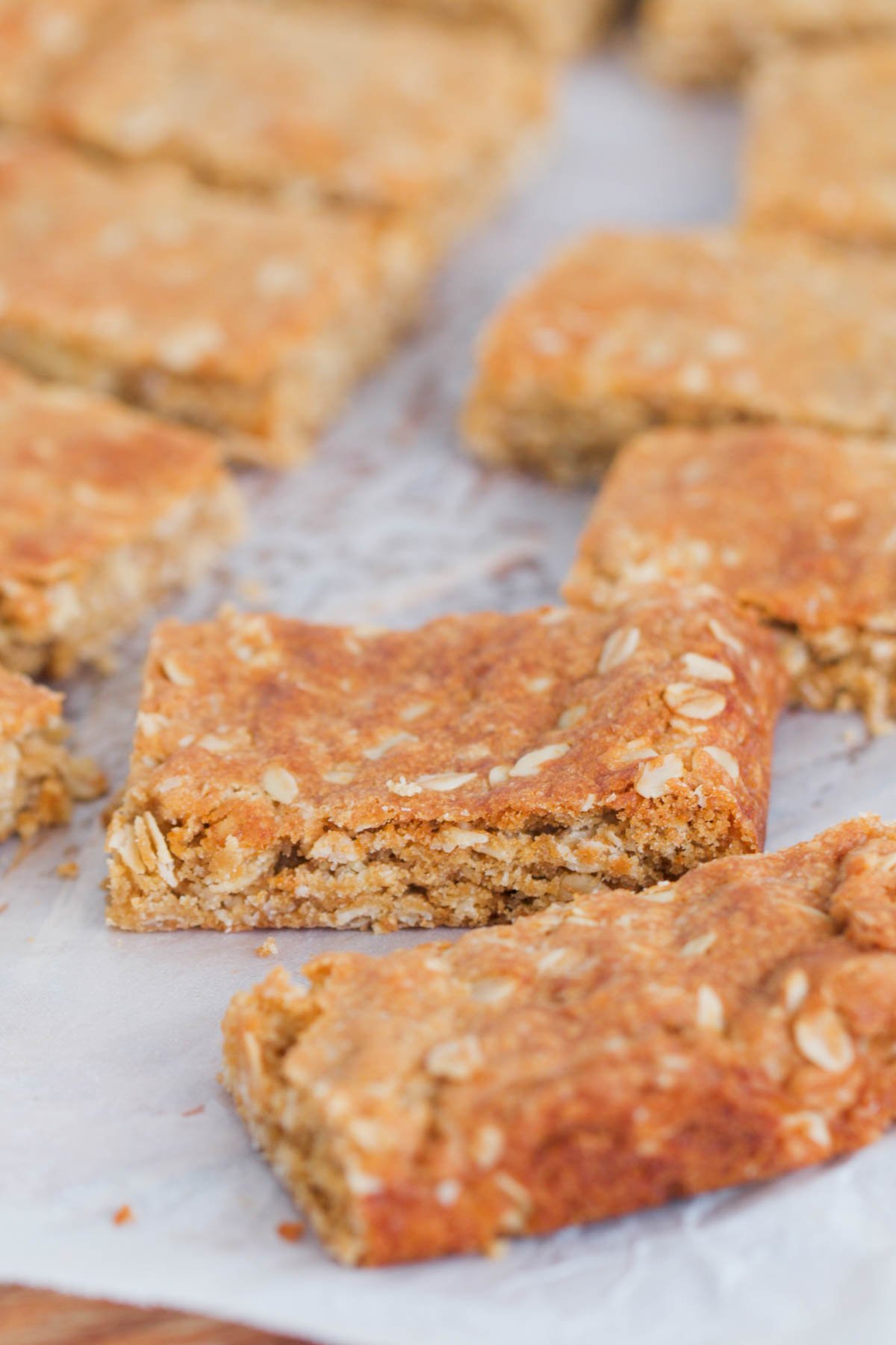 Pieces of sweet slice made with rolled oats on a chopping board with baking paper.