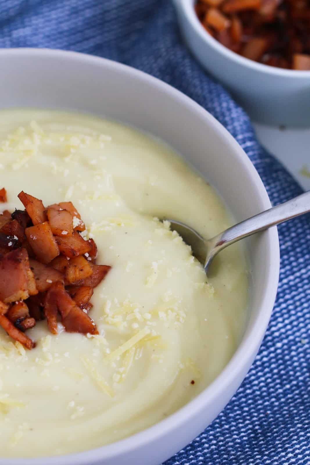 A spoon in a bowl of creamy soup with bacon.