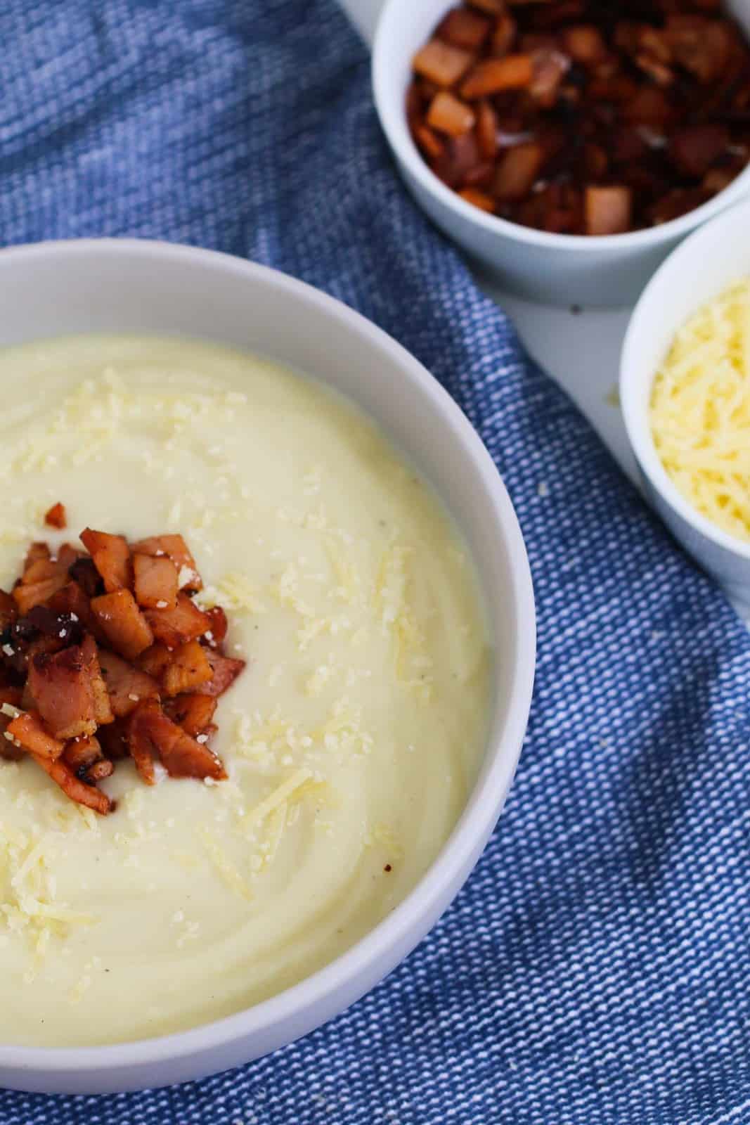 Pieces of crispy bacon on top of a bowl of cauliflower soup with parmesan cheese.