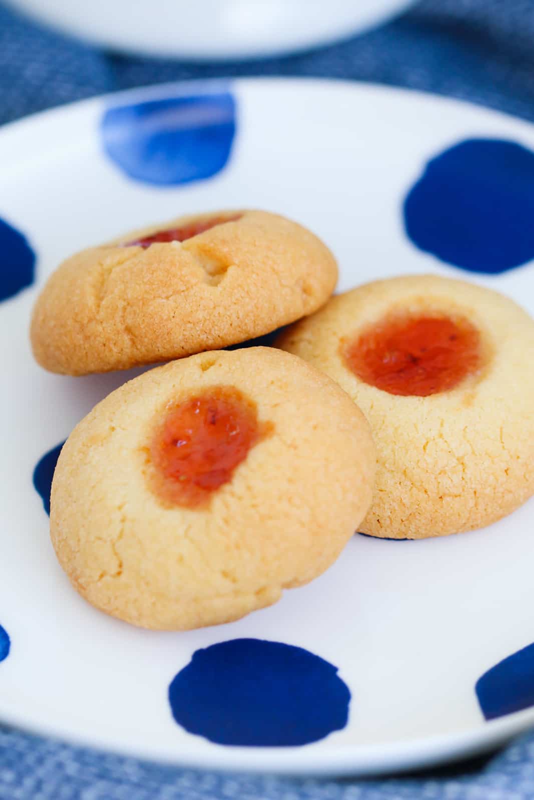 Three thumbprint cookies with strawberry jam on a blue and white plate.