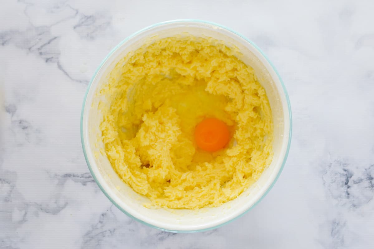 An egg added to creamed butter and sugar in a bowl. 