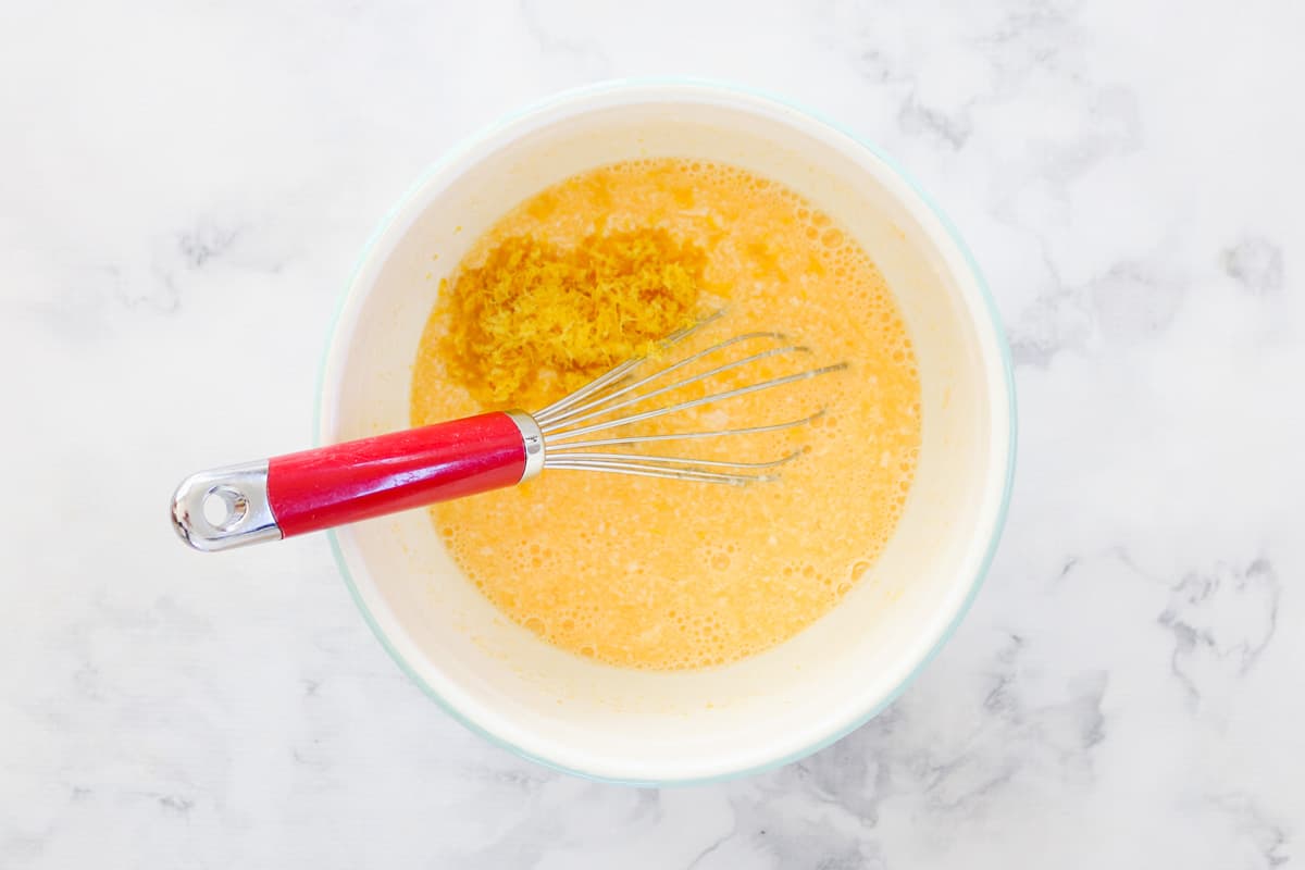 Lemon zest being added to a mixing bowl of yellow liquid. 