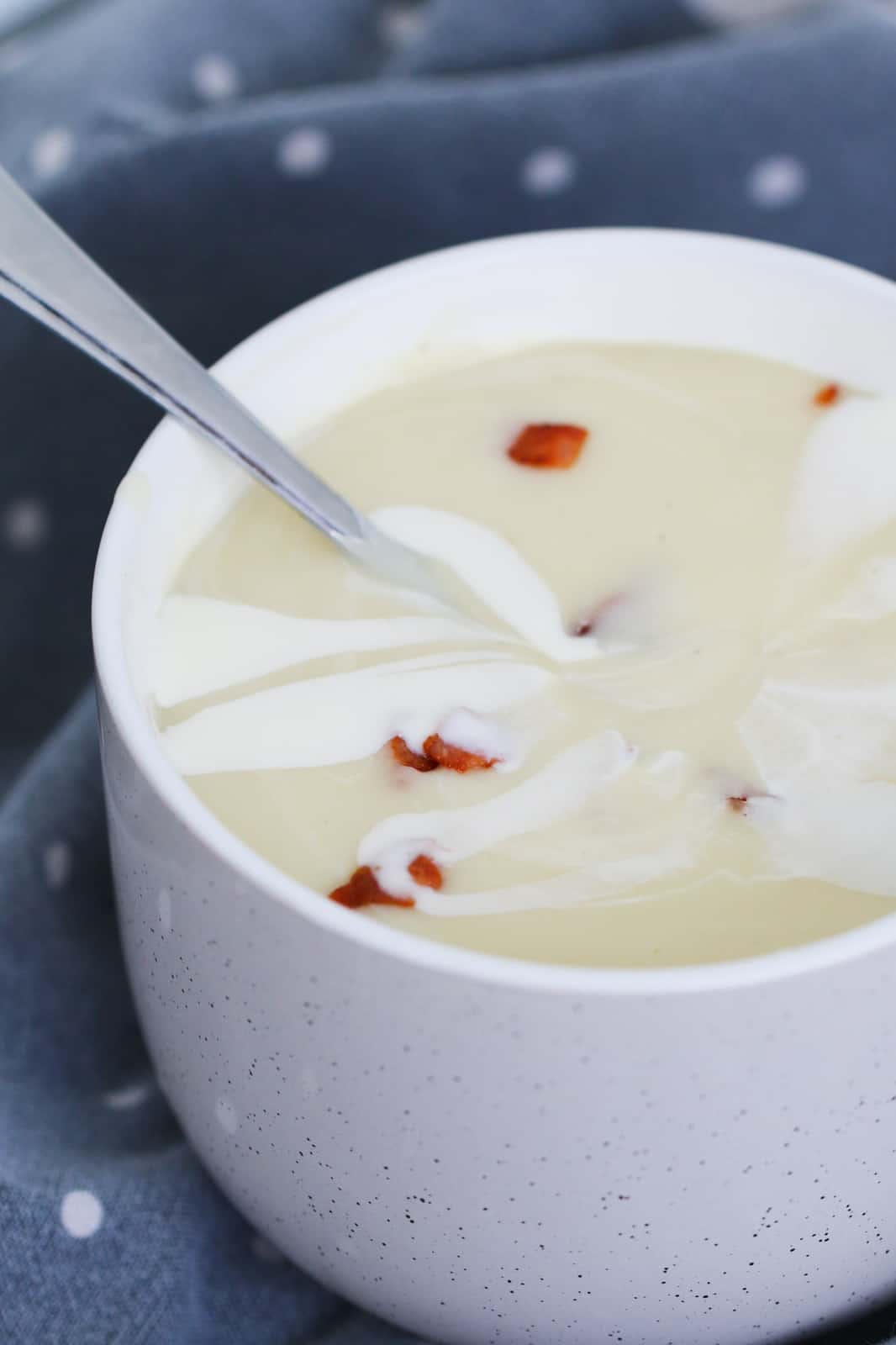 A spoon in a mug of healthy potato leek soup with cream and bacon.