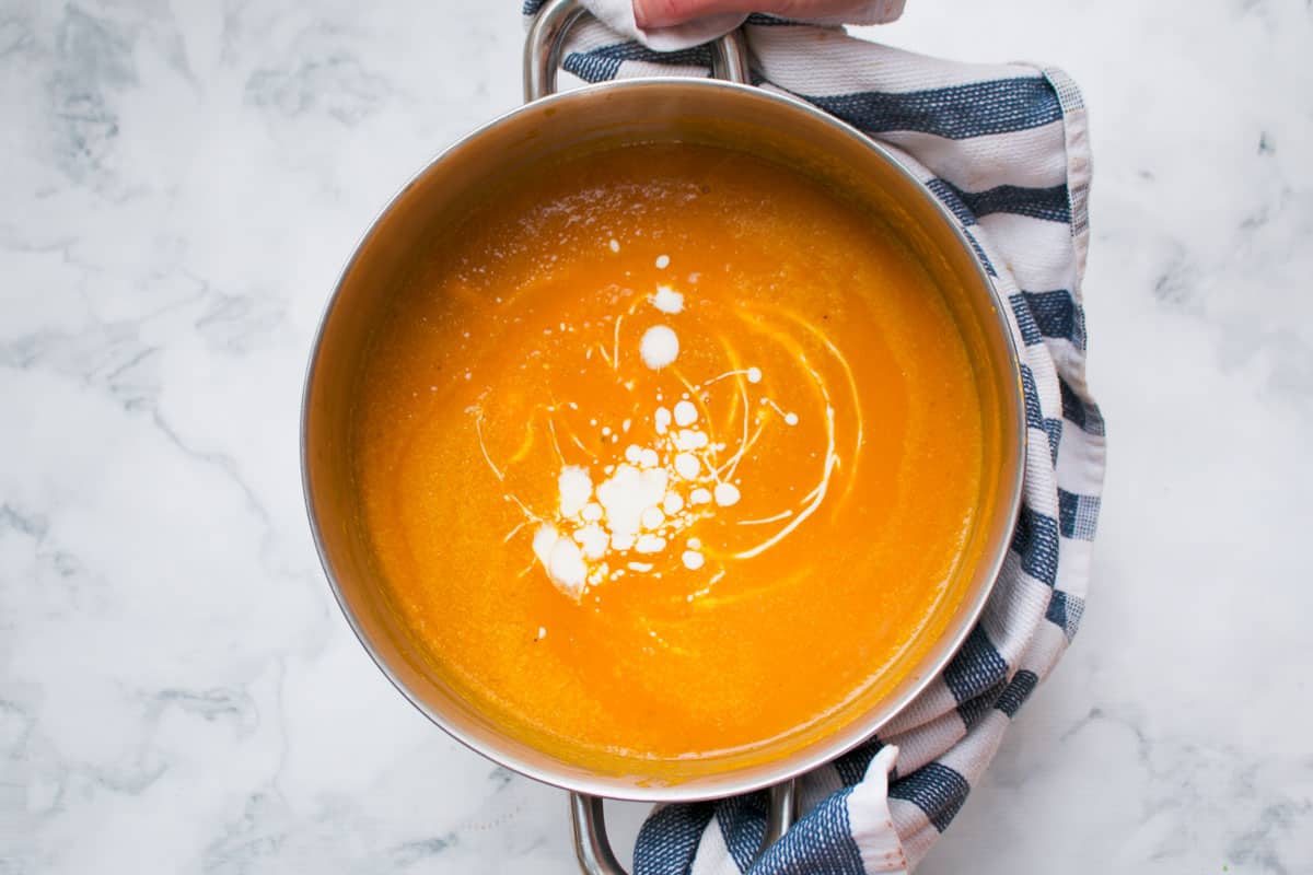 A saucepan of pumpkin soup drizzled with cream.