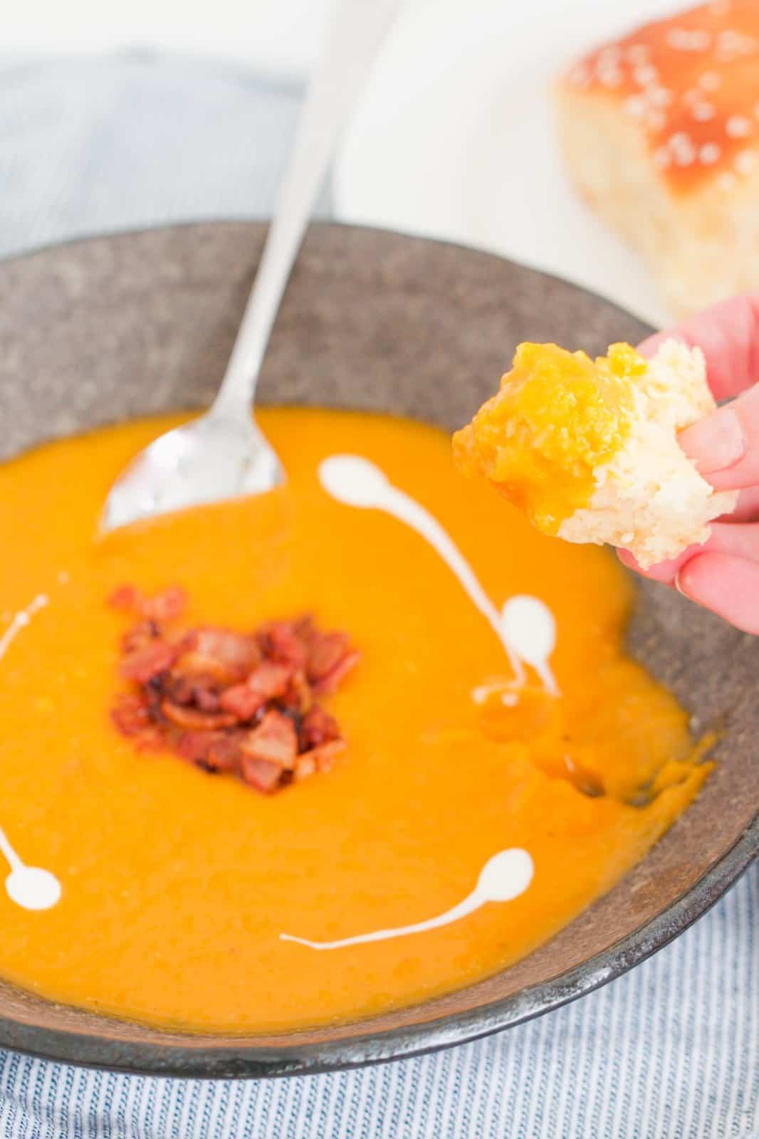 A hand holding a piece of bread being dipped into a bowl of soup.