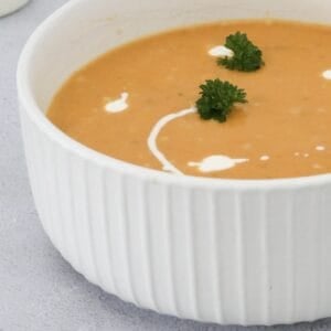 A bowl of roast pumpkin soup with cream swirls and parsley.