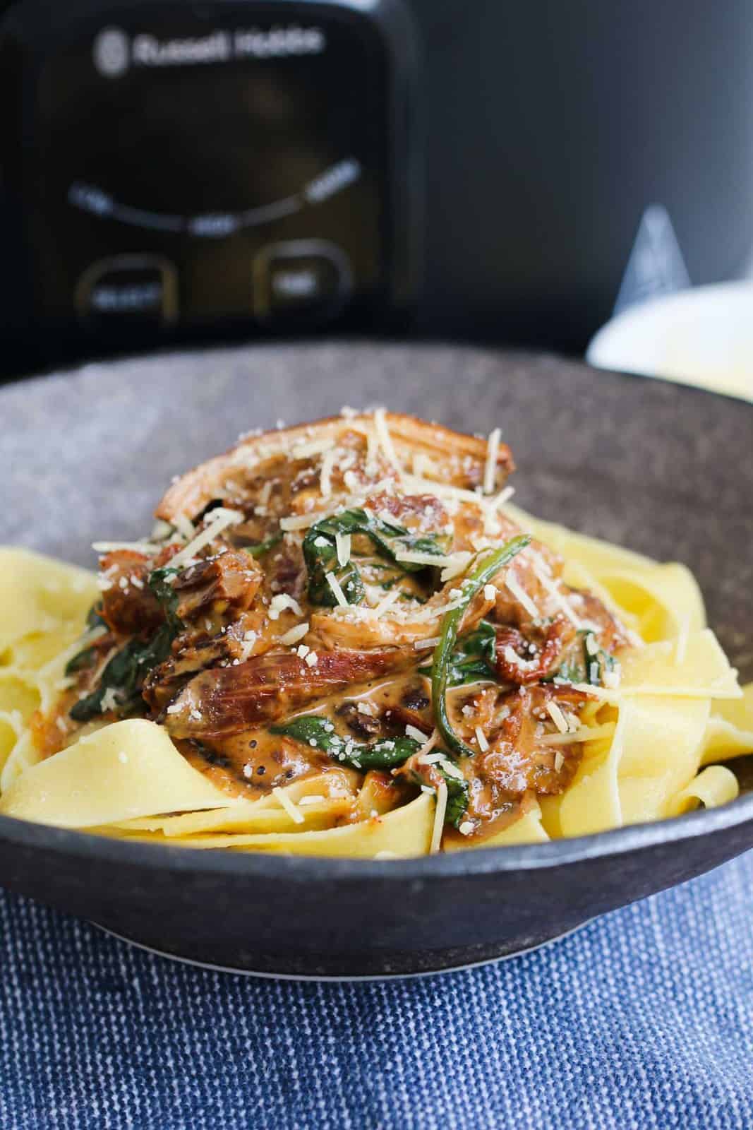 A bowl of pasta topped with creamy paprika chicken and parmesan.