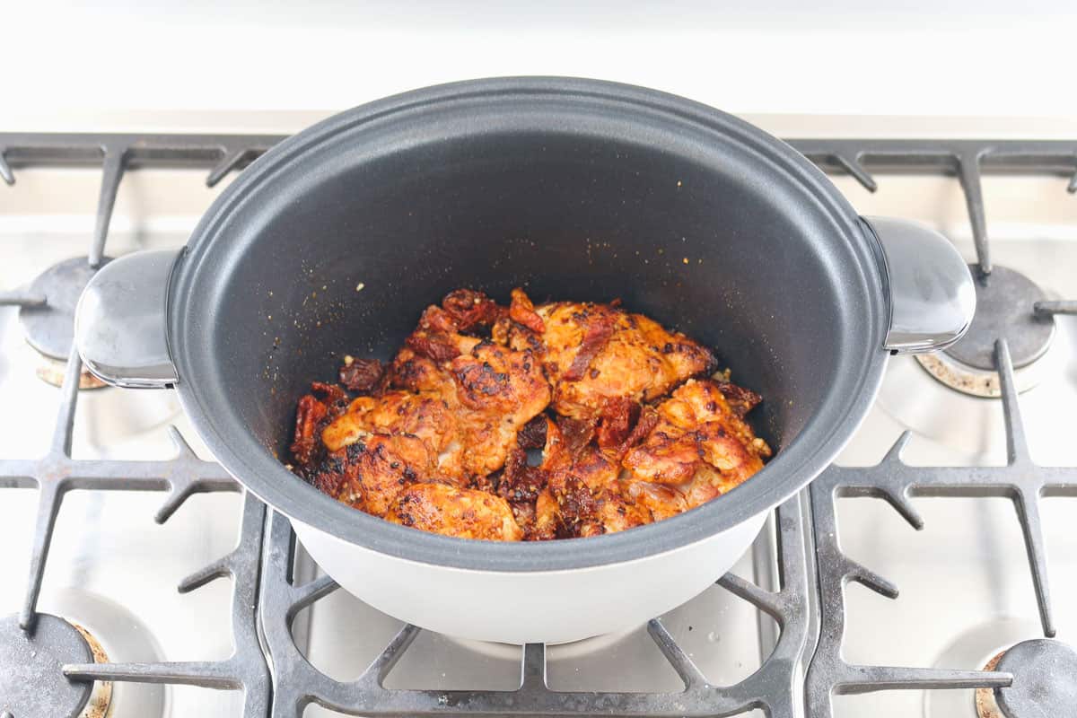 Chicken being seared on the stove-top in a slow cooker pot.