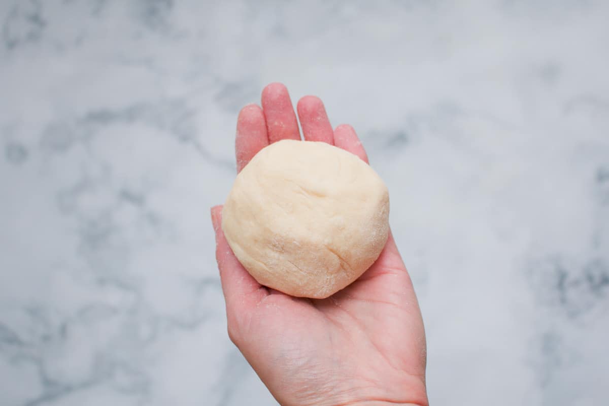 A round ball of homemade bread dough in a hand.