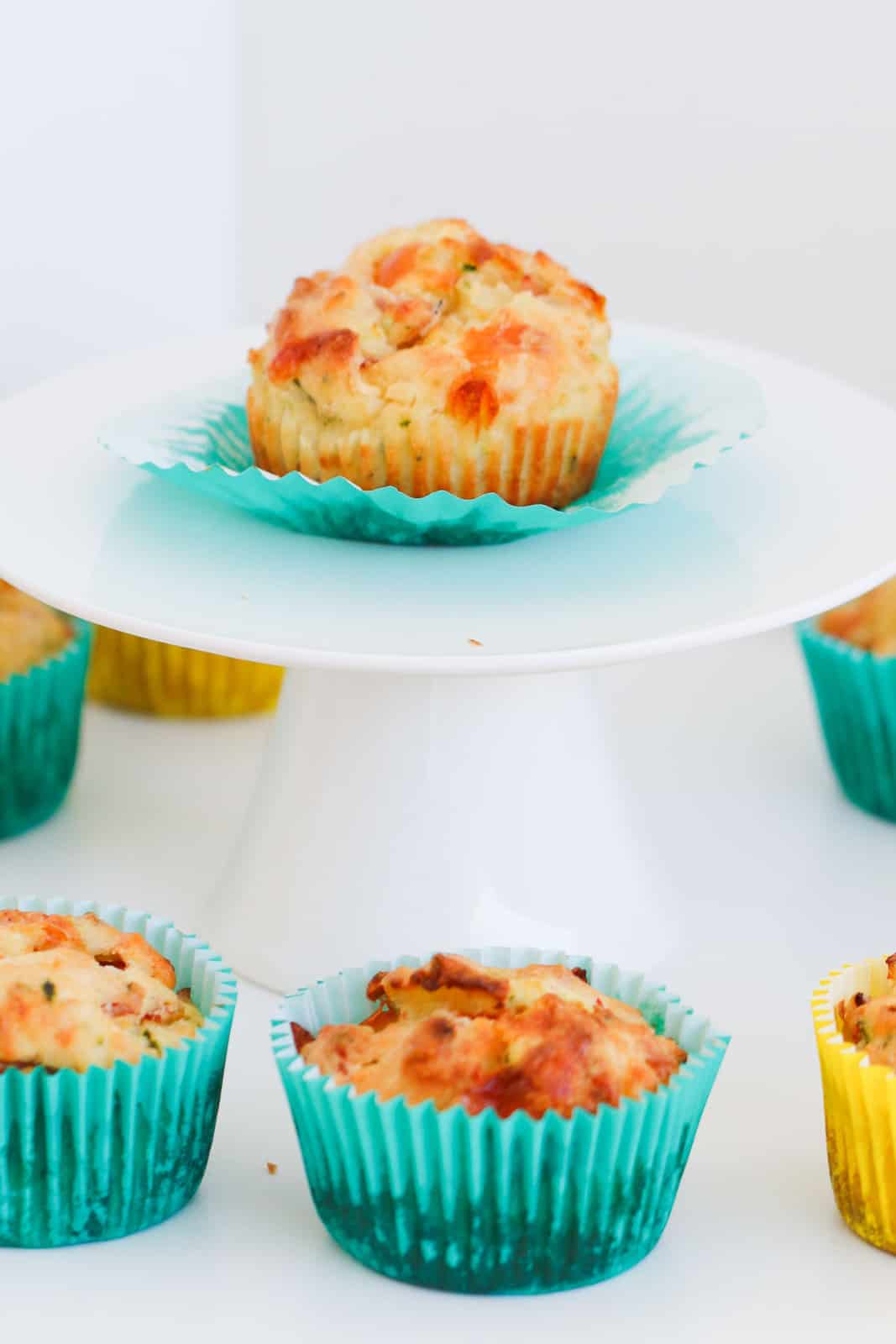 A savoury muffin on a white cake plate with more muffins in the background.