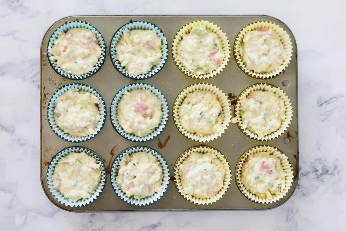 Savoury muffin mixture in a muffin tray.