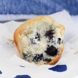 A half-eaten sweet white muffin with blueberries mixed throughout.