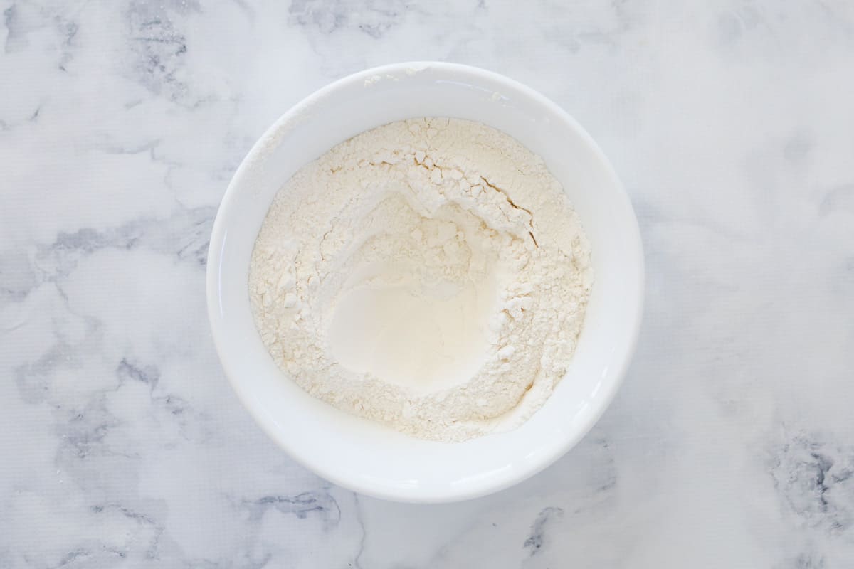 Flour and sugar in a white bowl with a well in the middle.
