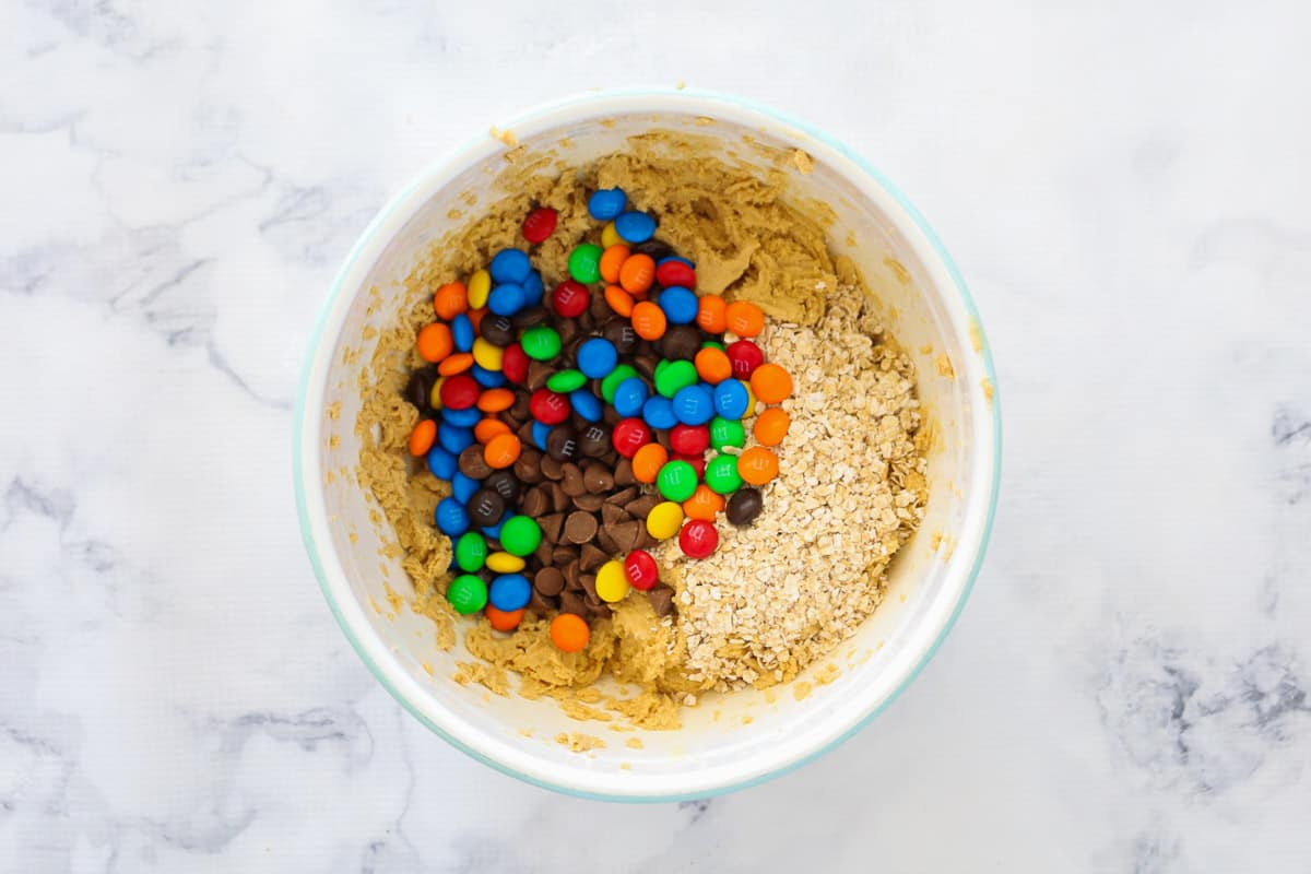 M&Ms and chocolate chips being added to a bowl of cookie dough.