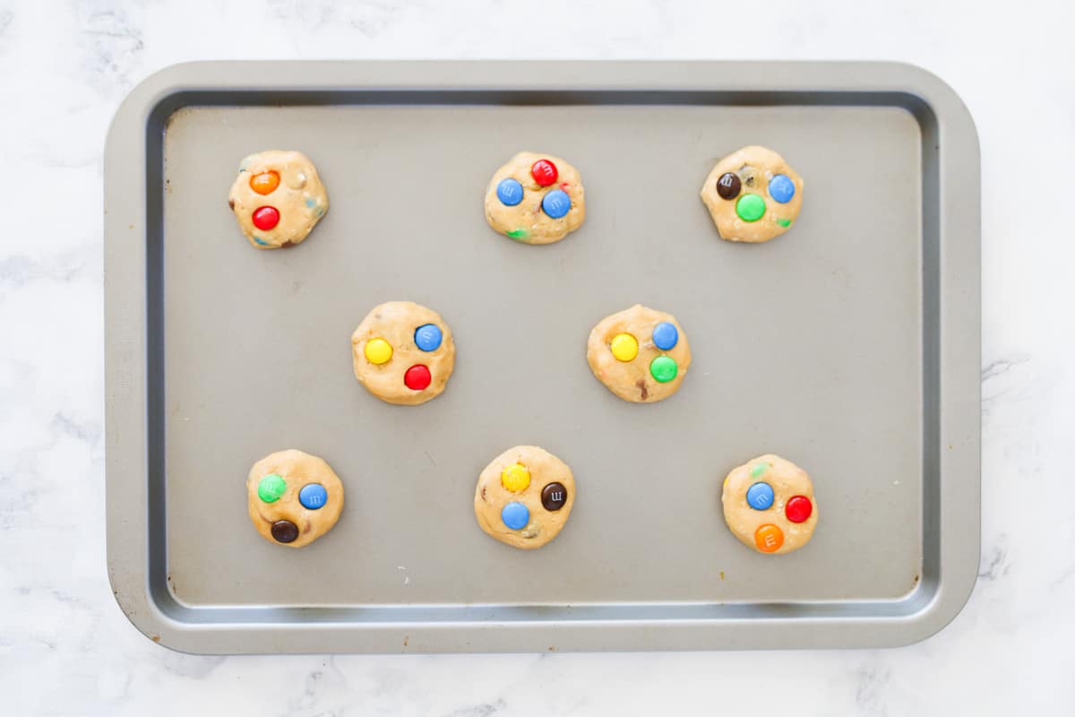 A tray of peanut butter cookies with bright coloured M&Ms on top.