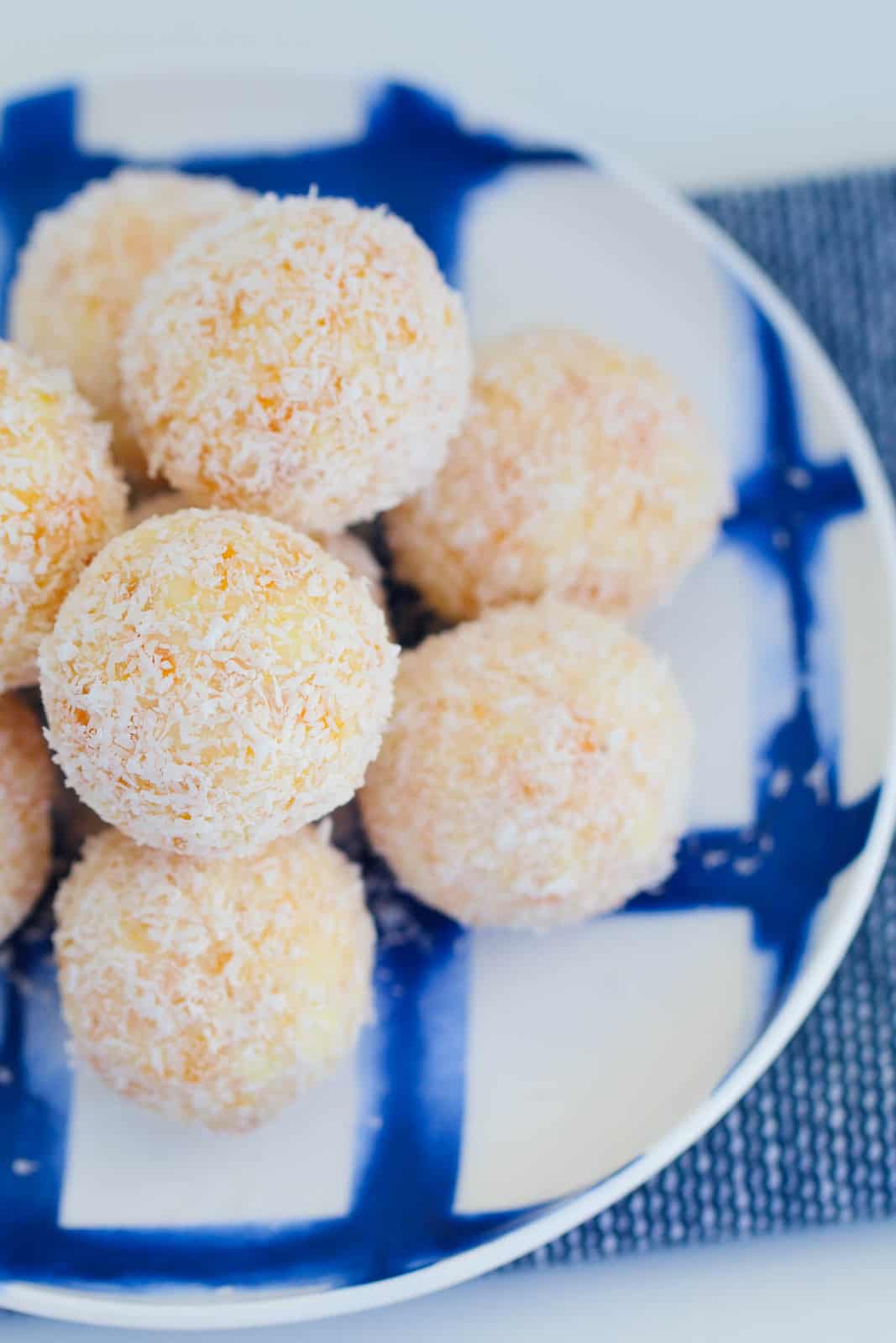 A downwards photo of a plate of coconut balls with chocolate and apricot on a blue and white plate.