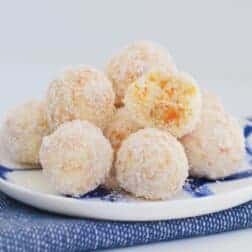 A blue and white striped plate topped with a pile of round balls covered in coconut.