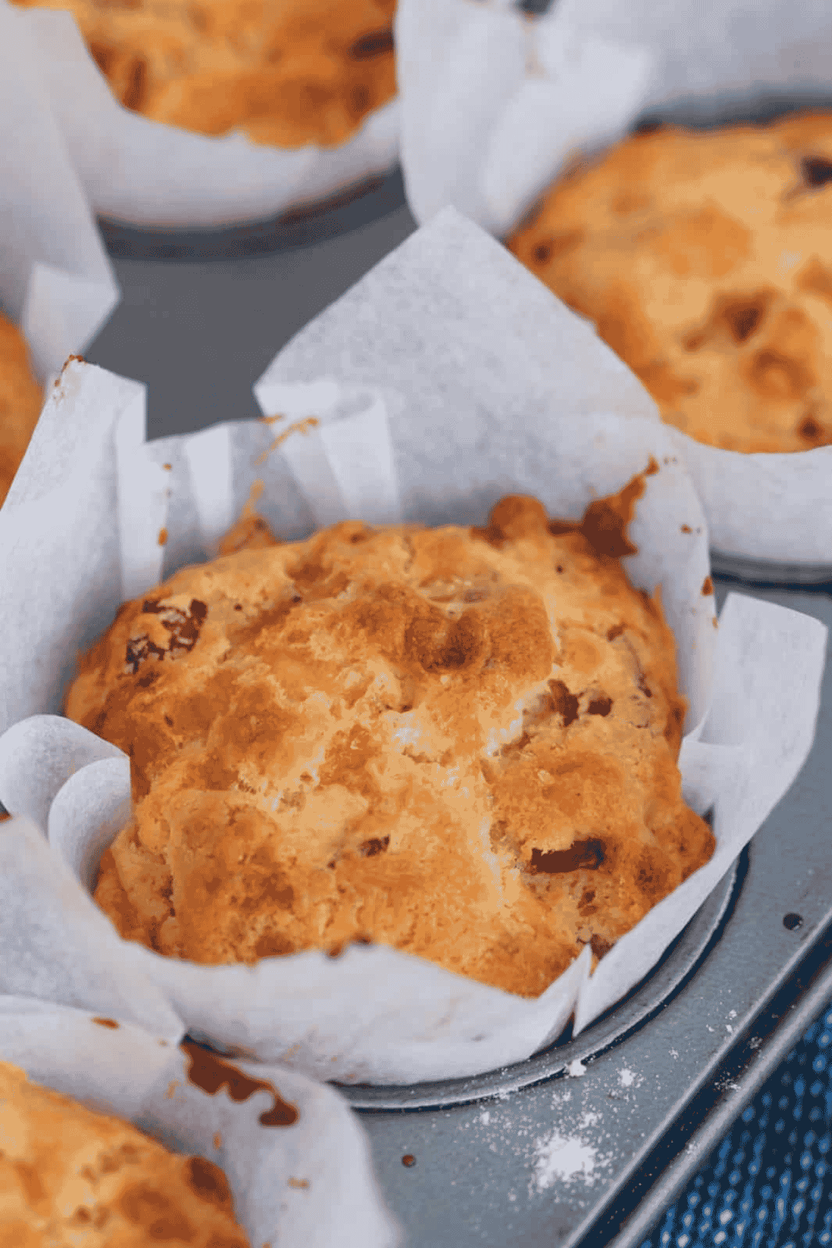 A golden crunchy topped cheese muffin with bacon pieces in a white paper case.