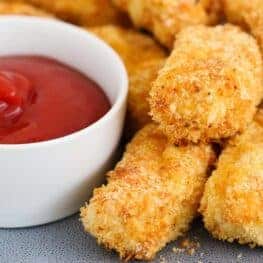 A stack of golden crunchy rectangular nuggets with red tomato sauce in a white bowl.