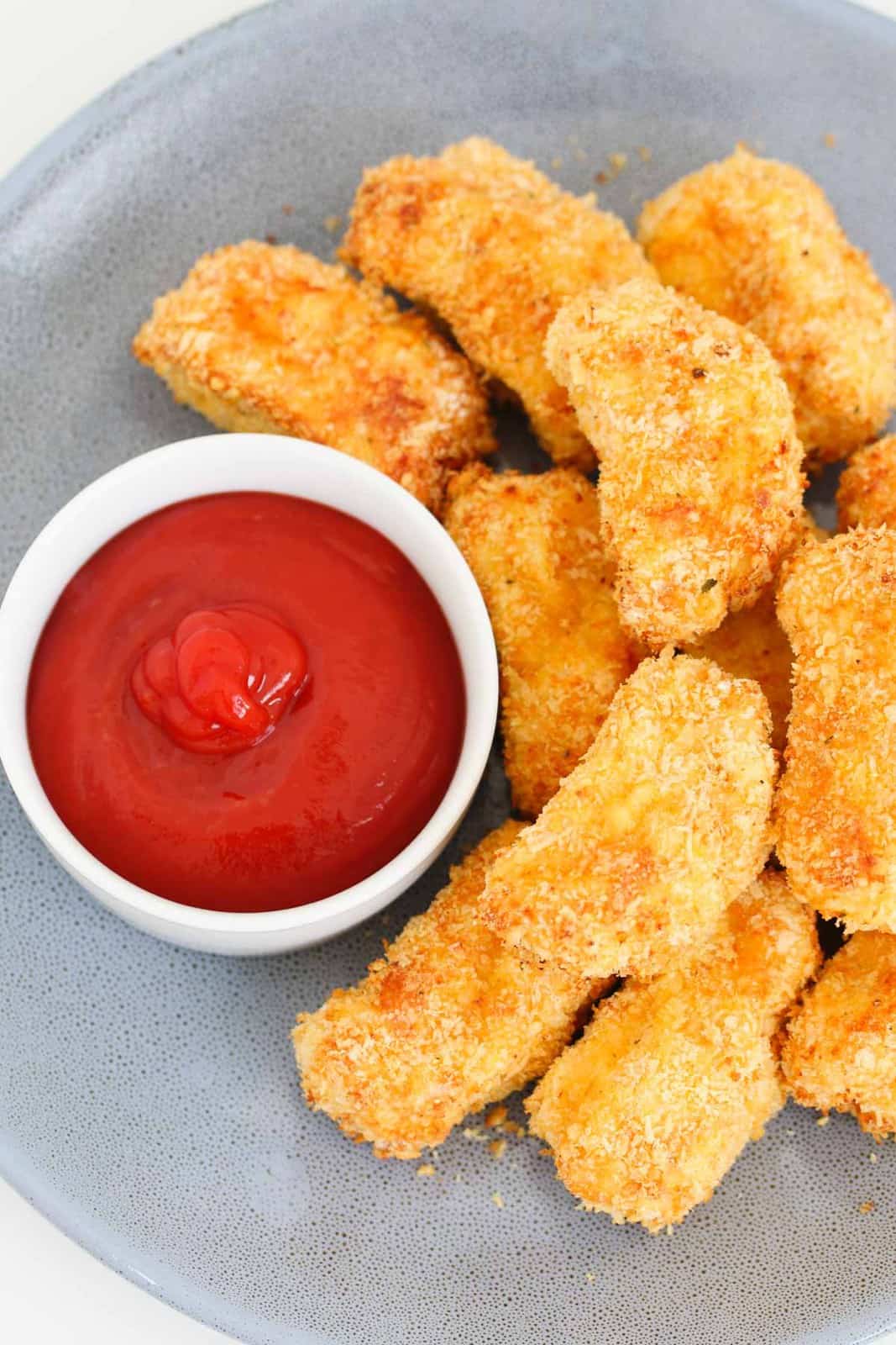 A plate of golden homemade chicken bites on a plate with a bowl of sauce.