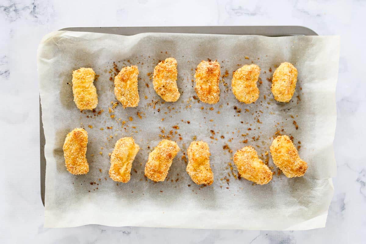 A baking tray covered with parchment paper with crumbed chicken bites.
