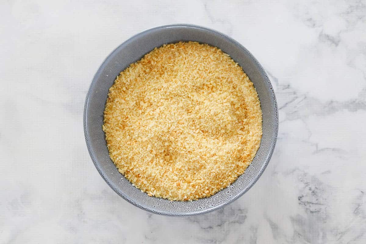 Panko crumbs mixed with chicken stock powder and grated parmesan in a blue bowl.