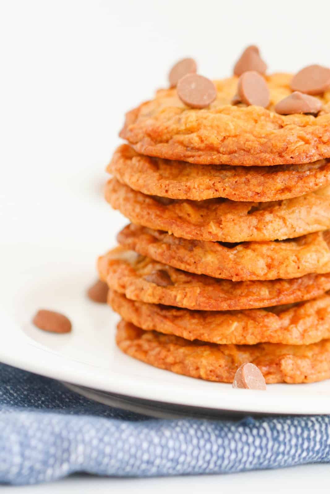 A stack of flat crispy chocolate chip cookies on a white plate.