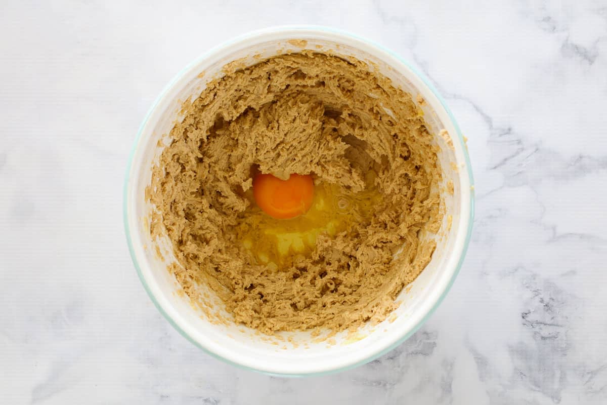 An egg in a mixing bowl with creamed butter and sugar.