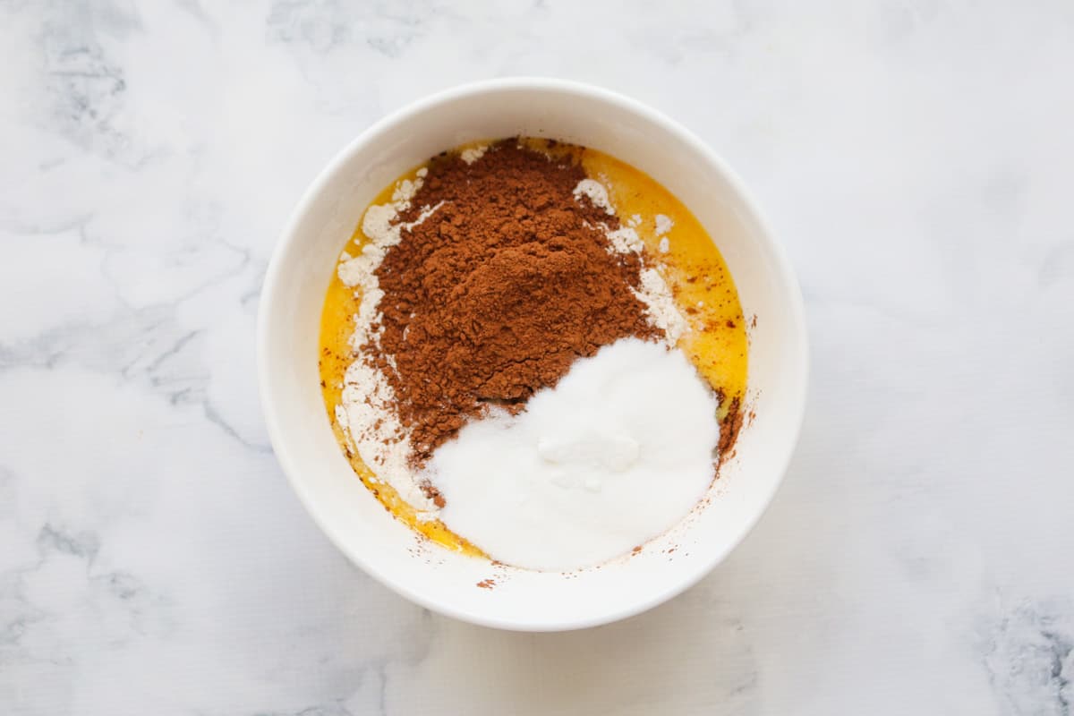 Self-raising flour, caster sugar and cocoa powder in a bowl of melted butter.