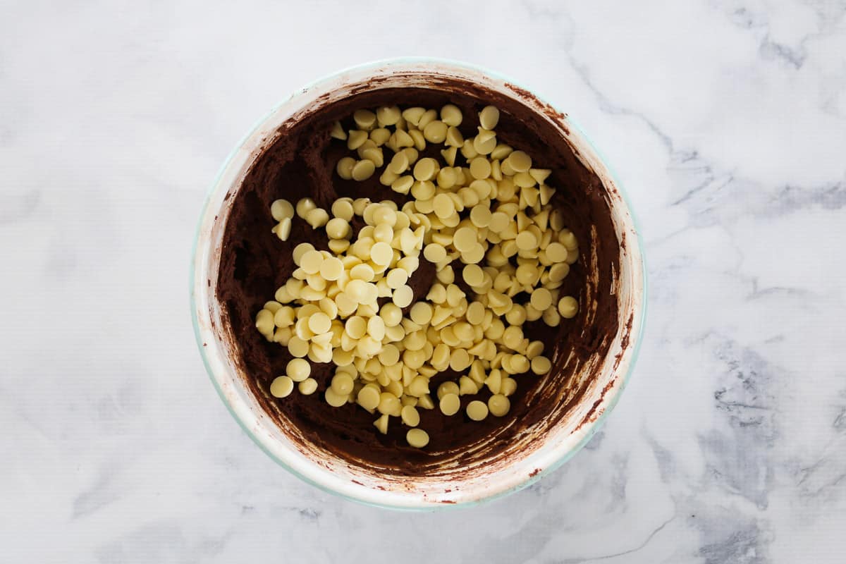 White chocolate chips on top of chocolate dough in a bowl.