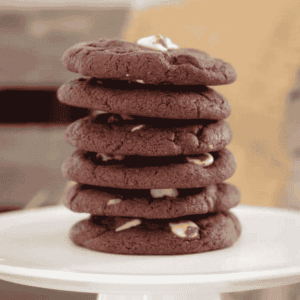 A tall stack of double chocolate chip cookies with white chocolate chunks, on a white plate.
