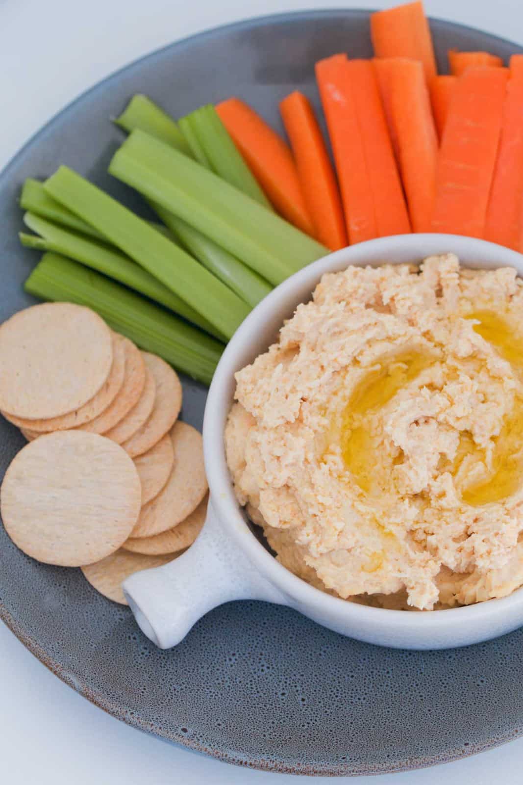 Crackers, carrot and celery around a bowl of smooth hummus.