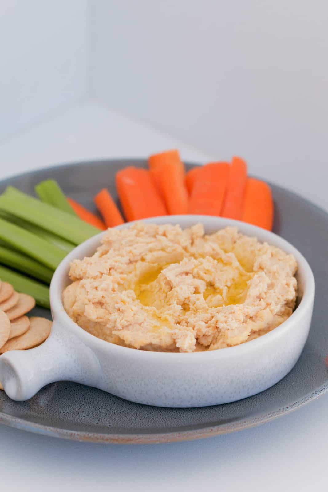 A bowl of Hummus Dip, drizzled with olive oil, served with carrot, celery and crackers