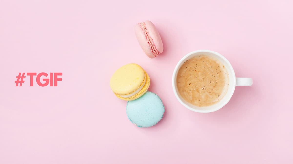 A cup of coffee with 3 colourful macarons on a pink background.